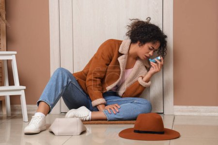 Téléchargez les photos : Jeune femme afro-américaine utilisant un inhalateur d'asthme près de la porte dans le hall - en image libre de droit