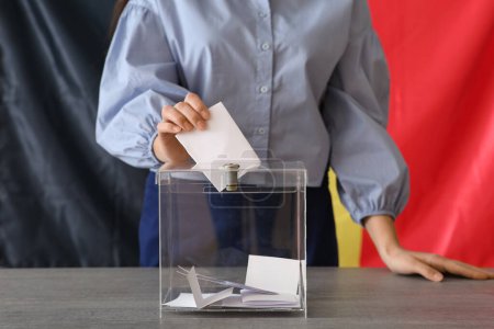 Voting young woman with Belgium flag near ballot box on table at polling station, closeup