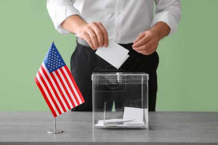 Voting young man with USA flag near ballot box on table at polling station, closeup