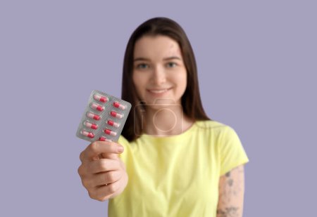 Young woman with blister of vitamin supplements on lilac background, closeup