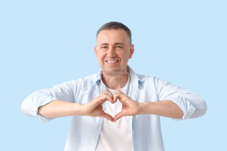 Téléchargez les photos : Mature homme faire coeur avec ses mains sur fond bleu - en image libre de droit