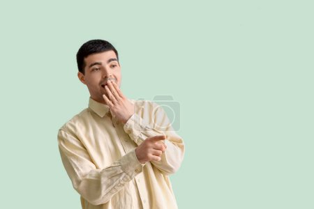 Photo for Surprised young man pointing at something on green background - Royalty Free Image
