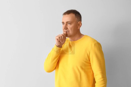 Photo for Mature man biting nails on light background - Royalty Free Image