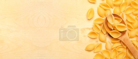 Heap of raw conchiglie pasta and spoon on wooden background with space for text