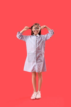 Funny little girl with magnifiers on red background