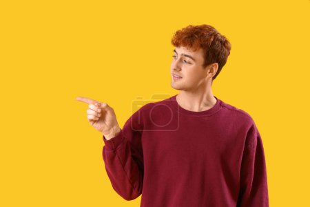 Téléchargez les photos : Jeune rousse homme pointant quelque chose sur fond jaune - en image libre de droit