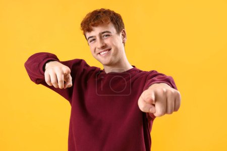 Téléchargez les photos : Jeune rousse homme pointant vers le spectateur sur fond jaune - en image libre de droit