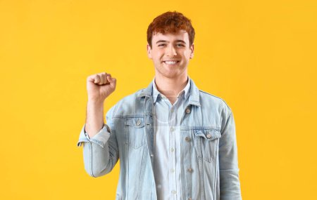 Téléchargez les photos : Jeune homme rousse avec poing serré sur fond jaune - en image libre de droit