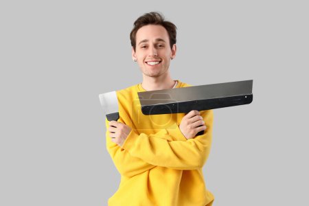 Young man with putty knives on light background