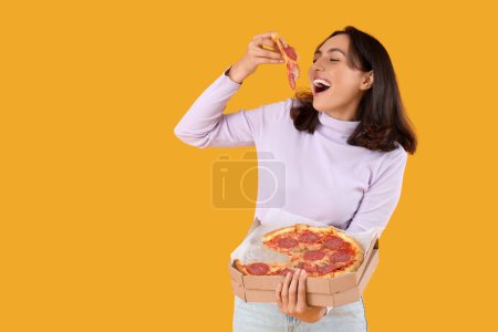 Junge Frau isst leckere Pfefferoni-Pizza auf gelbem Hintergrund