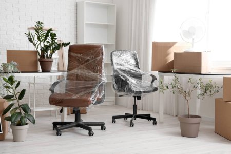 Téléchargez les photos : Intérieur du bureau avec des chaises enveloppées dans un film étirable et des boîtes en carton le jour du déménagement - en image libre de droit