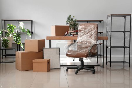 Téléchargez les photos : Intérieur du bureau avec chaise enveloppée dans un film étirable et des boîtes en carton le jour du déménagement - en image libre de droit