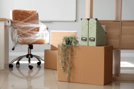 Téléchargez les photos : Intérieur du bureau léger avec chaise enveloppée dans un film étirable et des boîtes en carton le jour du déménagement - en image libre de droit