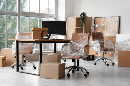 Téléchargez les photos : Intérieur du bureau moderne avec des chaises enveloppées dans un film étirable et des boîtes en carton le jour du déménagement - en image libre de droit