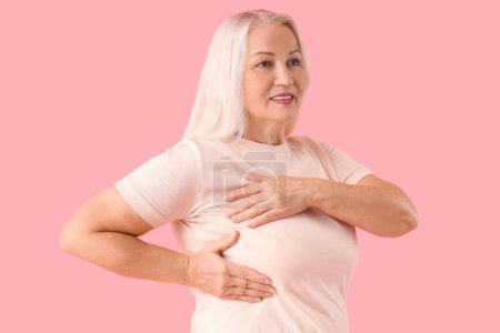 Ältere Frau überprüft ihre Brust auf rosa Hintergrund. Krebsaufklärungskonzept