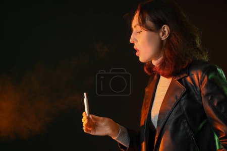 Téléchargez les photos : Jeune femme fumant cigare électronique sur fond sombre - en image libre de droit