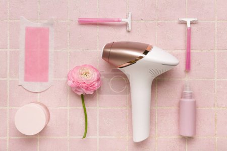 Moderner Photoepilator mit Wachsstreifen, Rasierern und Kosmetikprodukten auf rosa Fliesenhintergrund