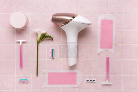 Photo for Modern photoepilator with wax strips, razors and jar of cream on pink tile background - Royalty Free Image