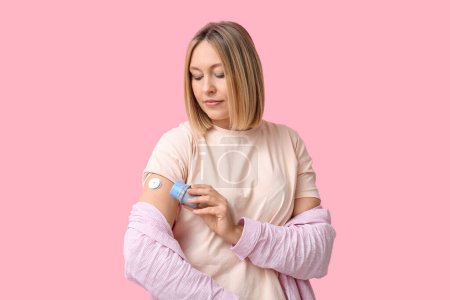Woman with glucose sensor for measuring blood sugar level and applicator on pink background. Diabetes concept