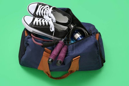 Sports bag with sportswear and fitness equipment on green background