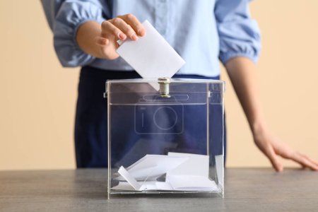 Voting young woman near ballot box on table at polling station, closeup