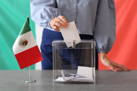 Voting young woman with Mexican flag near ballot box on table at polling station, closeup