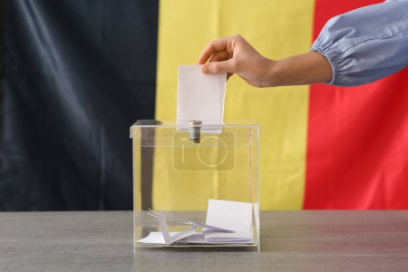 Voting woman with Belgium flag near ballot box on table at polling station