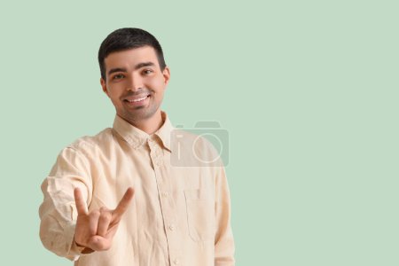 Photo for Young man showing "devil horns" on green background - Royalty Free Image