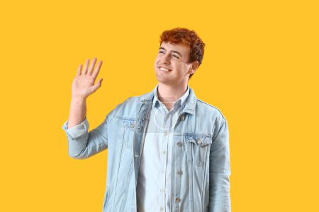 Téléchargez les photos : Jeune rousse homme agitant la main sur fond jaune - en image libre de droit