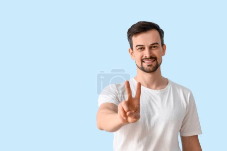 Photo for Handsome man showing victory gesture on blue background - Royalty Free Image