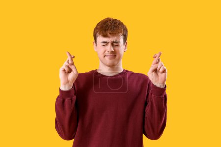 Téléchargez les photos : Inquiète jeune rousse homme croisant les doigts sur fond jaune - en image libre de droit
