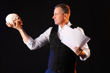Photo for Mature actor with skull reading script on dark background - Royalty Free Image