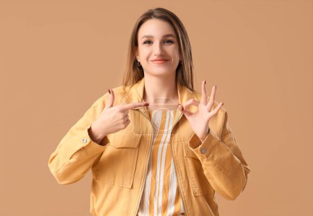 Téléchargez les photos : Jeune femme pointant vers OK geste sur fond brun - en image libre de droit