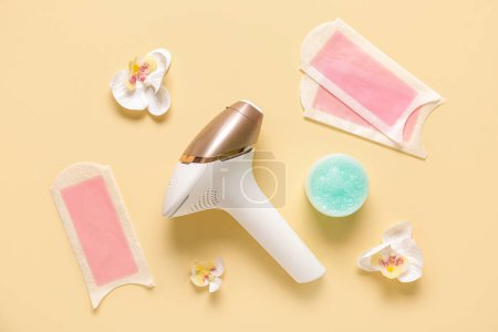 Photo for Modern photoepilator with wax strips, jar of scrub and orchid flowers on yellow background - Royalty Free Image