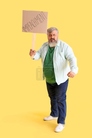 Téléchargez les photos : Protestant homme mûr tenant la plaque avec le mot IMPEACHMENT sur fond jaune - en image libre de droit