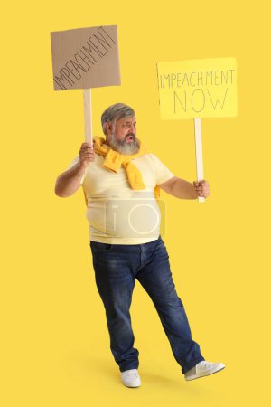 Téléchargez les photos : Protestant homme mûr tenant des pancartes avec le mot IMPEACHMENT sur fond jaune - en image libre de droit