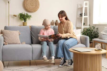 Téléchargez les photos : Petite fille après la chimiothérapie avec sa mère lisant le livre à la maison. Journée internationale du cancer chez les enfants - en image libre de droit