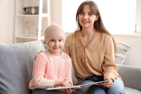 Téléchargez les photos : Petite fille après la chimiothérapie avec sa mère lisant le livre à la maison. Journée internationale du cancer chez les enfants - en image libre de droit