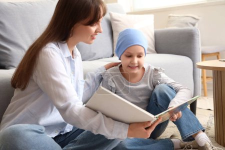 Téléchargez les photos : Petite fille après la chimiothérapie avec sa mère lisant l'histoire à la maison. Journée internationale du cancer chez les enfants - en image libre de droit