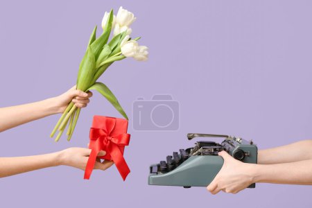 Manos femeninas con máquina de escribir retro, caja de regalo y flores de tulipán para el Día Internacional de la Mujer sobre fondo lila, primer plano
