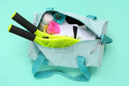 Photo for Sport bag with sportswear and badminton rackets on cyan background - Royalty Free Image