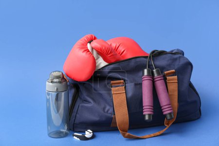 Sports bag with bottle and boxing gloves on blue background