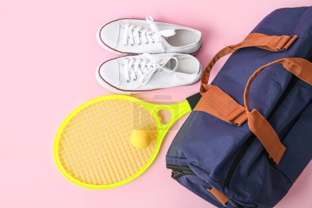 Sporttasche mit Sportbekleidung, Tennisschläger und Schuhen auf rosa Hintergrund