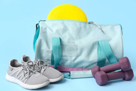 Sports bag with sportswear and workout equipment on blue background
