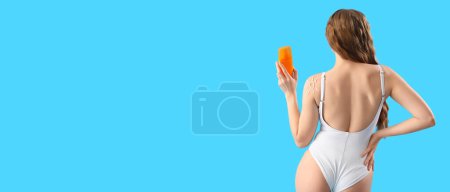 Beautiful young woman in swimsuit holding sunscreen cream on light blue background with space for text, back view
