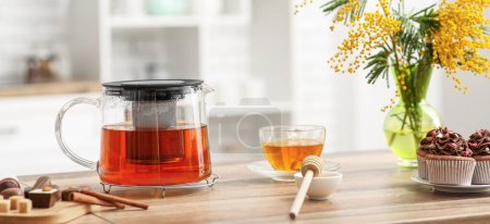Foto de Tetera y taza de té negro con dulces y miel en la mesa en la cocina - Imagen libre de derechos