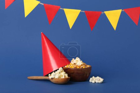Spoon with bowl of corn, party hat and flags on blue background. Festa Junina (June Festival) celebration