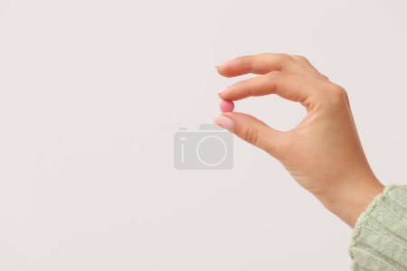 Woman holding pink pill on white background