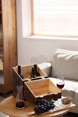 Téléchargez les photos : Boîte en bois avec vin et collations sur la table dans le salon - en image libre de droit