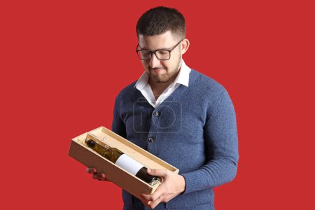 Photo for Young sommelier holding box with bottle of wine on red background - Royalty Free Image